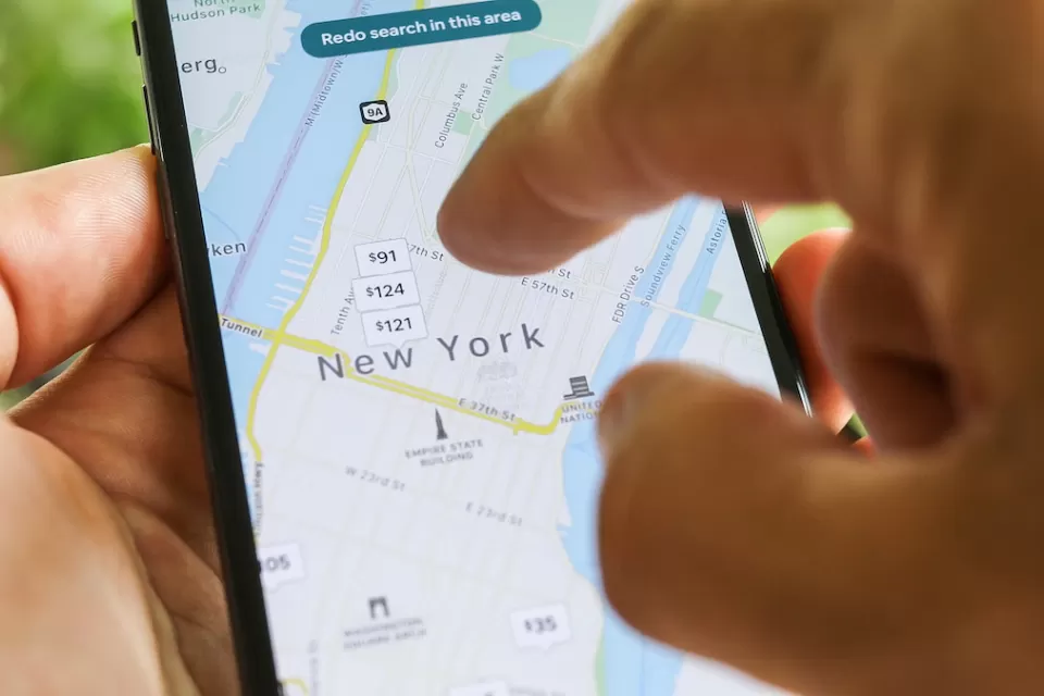 Close-up of hand using smartphone to search New York City map on Airbnb app.